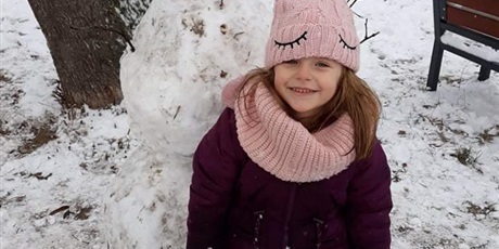 Powiększ grafikę: Zimowe zdjęcie dziecka  na przedszkolnym placu zabaw z bałwankiem