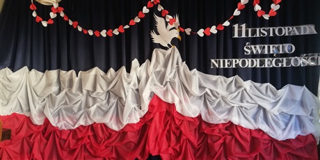 Powiększ grafikę: W tle bialo czerwona flaga Polski z trzymającym ją ptakiem orłem i napis 11 listopada na granatowym tle