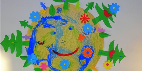 Powiększ grafikę: Plakat papierowy ziemi z zielonymi choinkami ,niebieskimi kwiatkami i luddzikmi wykonany przez dzieci w wieku przedszkolnym. 