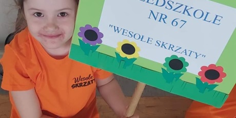 Powiększ grafikę: Na zdjęciu dziewczynka w pomarańczowej bluzce z  tablicą z napisem przedszkole  nr 67 Wesołe Skrzaty