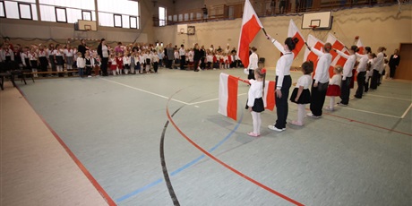 Powiększ grafikę: Na zdjęciu grupa dzieci w strojach biało czerwonych z flagami w dłoni  podczas występu z okazji Święta Niepodległośc