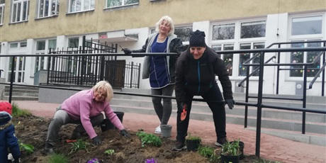 Powiększ grafikę: Na zdjęciu grupa ludzi sadząca kwiaty wiosenne w ziemi na górce.