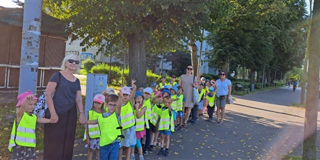 Powiększ grafikę: Na zdjęciu grupa dzieci w wieku przedszkolnym w odblaskowych kamizelka podczas spaceru na skrzyżowanie 