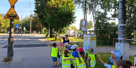 Powiększ grafikę: Na zdjęciu grupa dzieci w wieku przedszkolnym w odblaskowych kamizelka podczas spaceru na skrzyżowanie 