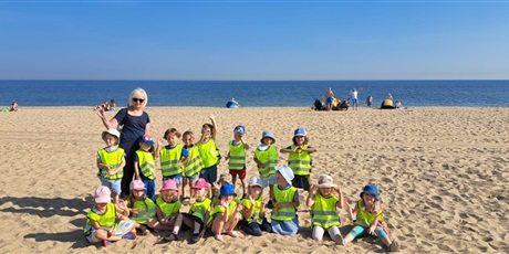 Powiększ grafikę: Na zdjęciu grupa dzieci w wieku przedszkolnym w odblaskowych kamizelkach podczas zabaw na plaży.