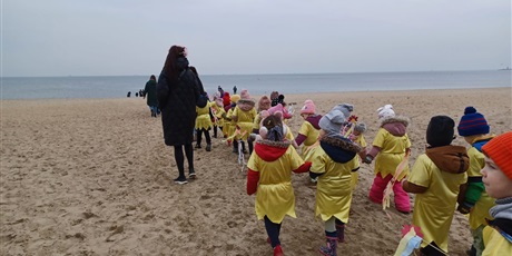 Powiększ grafikę: Na  zdjęciu grupa dzieci w wieku przedszkolnym w kolorowych strojach na plaży podczas witania pani Wiosny.