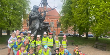 Powiększ grafikę: Grupa dzieci w wieku przedszkolnym w żółtych kamizelkach przy pomniku Jana Heweliusza.